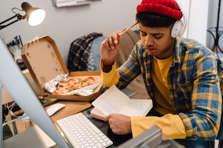Middle-eastern teenage boy using desktop computer while studying at home