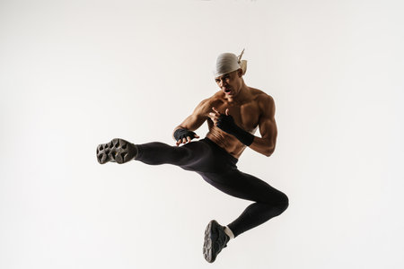 Young shirtless sportsman kicking and jumping while working out isolated over white background