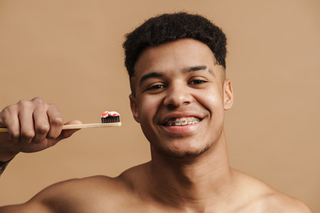 Young shirtless man smiling while posing with toothbrush isolated over beige backgroundの写真素材