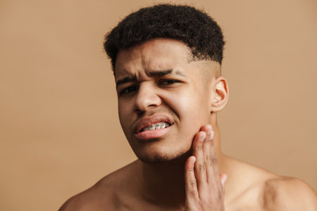 Young shirtless man frowning while touching his face isolated over beige backgroundの写真素材