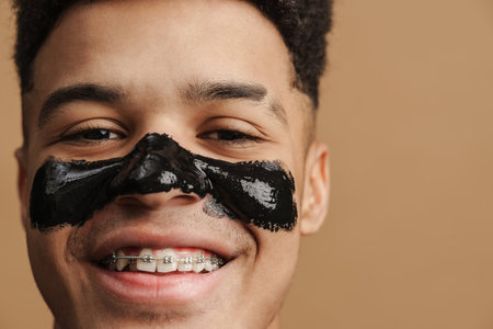 Young shirtless man with cosmetic mask smiling at camera isolated over beige backgroundの写真素材
