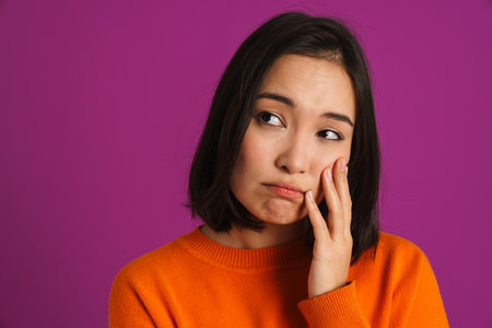 Young asian woman wearing sweater frowning and looking aside isolated over purple backgroundの写真素材