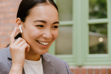 Asian woman in earphones listening music while sitting in cafe outdoorsの写真素材