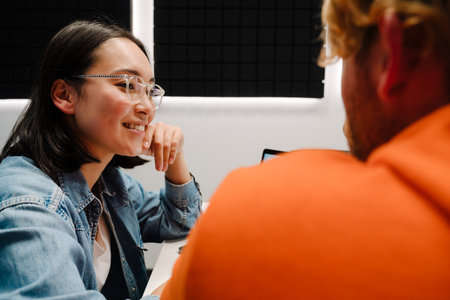 Happy young man and woman smiling and using laptop while broadcasting in radio studioの写真素材