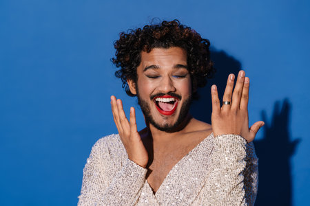 Young excited man with makeup laughing at camera isolated over blue background