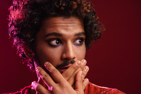 Young scared man with makeup covering his mouth and looking aside isolatedの写真素材