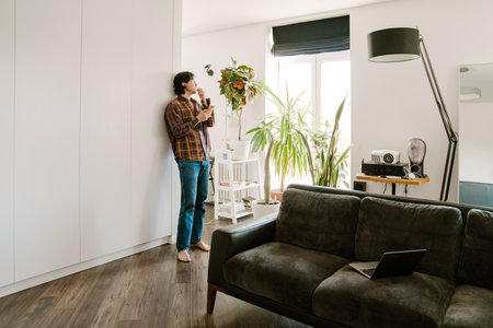 White man laughing and using mobile phone while standing at homeの写真素材