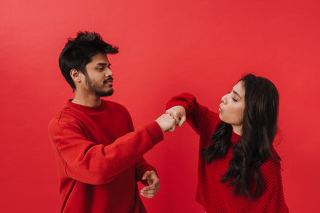 Young indian couple laughing and bumping their fists while posing together isolated over red...