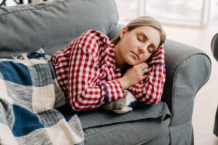 Young white relaxed woman wearing pajama sleeping on sofa at home in morning