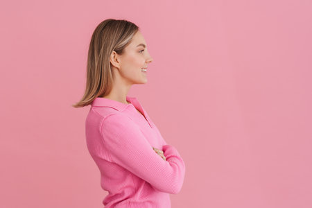 Young beautiful smiling girl with folded arms standing with her right side over isolated pink backgroundの写真素材