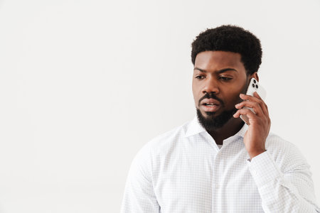 Black mid man wearing shirt talking on mobile phone isolated over white backgroundの写真素材
