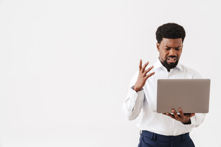 Black displeased man gesturing while working with laptop isolated over white backgroundの写真素材