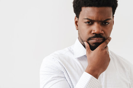 Black mid man wearing shirt holding his chin and looking at camera isolated over white backgroundの写真素材