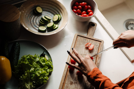 Up view of female hands cutting tomato on wooden boardの写真素材