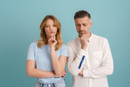 White puzzled couple frowning and looking away isolated over blue background