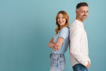 White happy man and woman smiling while standing back to back isolated over blue background