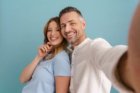 White young man and woman smiling and taking selfie photo together standing isolated over blue backgroundの写真素材