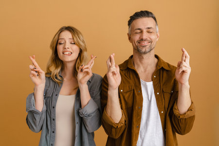 White happy woman and man smiling while standing with finger crossed isolated over yellow background