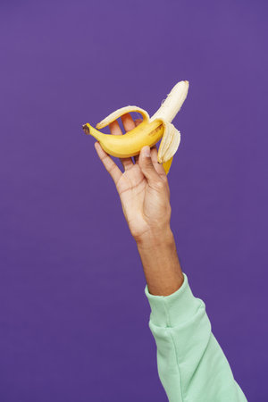 Black man's hand holding and showing banana at camera isolated over purple background
