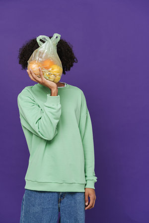 Young caribbean man holding and showing plastic bag with fruits isolated over purple background