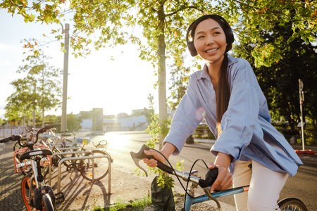 Asian woman in headphones smiling while riding bicycle on city street