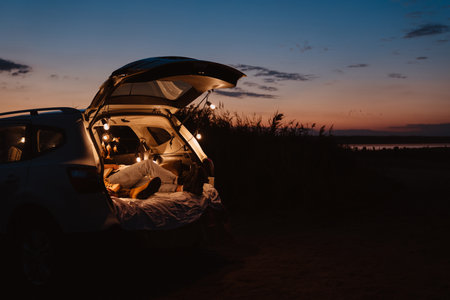 Happy young couple lying together in car by seaside in eveningの写真素材