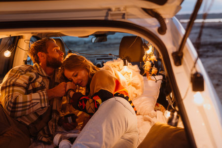 Happy young white couple smiling and lying together in car by seaside in evening