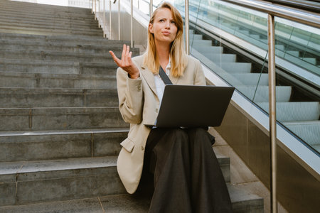 Young white serious woman using laptop while sitting on stairs outdoorsの写真素材