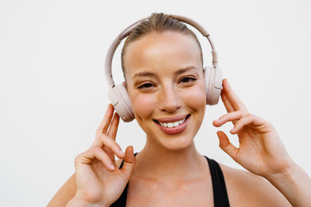 White young woman in headphones listening music while standing by wall outdoors