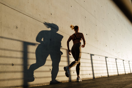 White young blond woman in tracksuit running by wall during workout outdoors