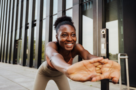 Young beautiful sporty smiling happy african woman stretching her back bending over with intertwined...