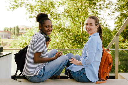 Young multiracial women smiling and using cellphone while sitting at parkの写真素材
