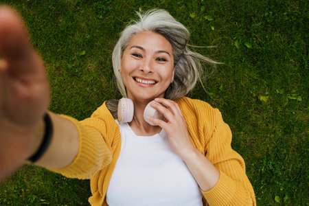 Grey asian woman laughing and taking selfie photo in summer park