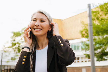 Grey asian woman laughing and talking on cellphone at city streetの写真素材
