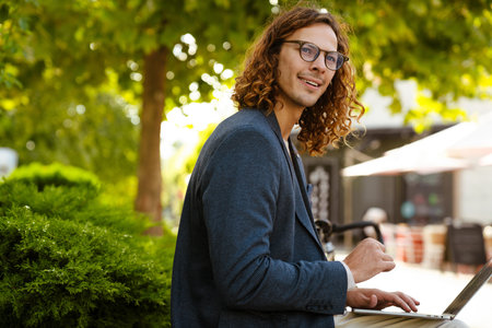 Ginger european man working with laptop while sitting in summer park