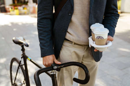 Ginger european man wearing jacket walking with bicycle and coffee on city streetの写真素材