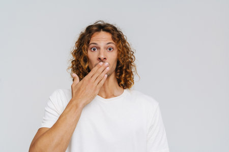 Ginger european man covering his mouth while expressing surprise isolated over white backgroundの写真素材