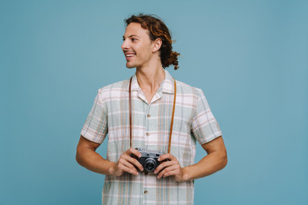 Ginger european man smiling while posing with retro camera isolated over blue backgroundの写真素材