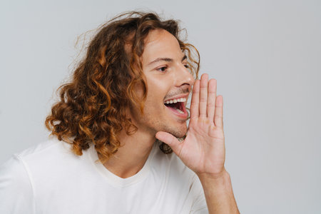 Ginger european man with curly hair smiling and calling someone isolated over white backgroundの写真素材