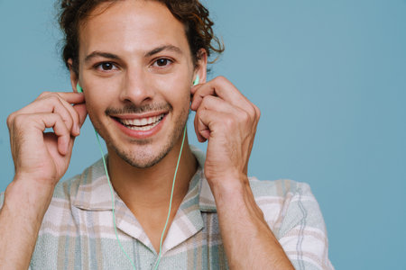 Ginger european man in earphones smiling and listening music isolated over blue backgroundの写真素材