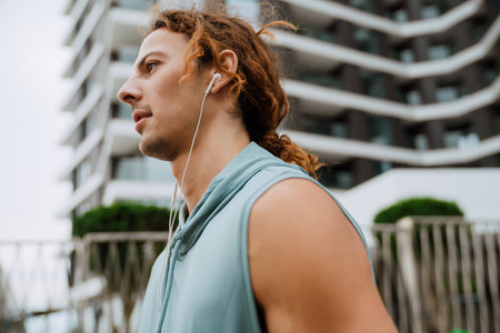 Profile portrait of young handsome long-haired man in headphones looking aside, while standing outdoorsの写真素材