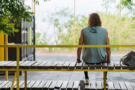 Young athletic long-haired man sitting with his back on athletic field outdoorsの写真素材