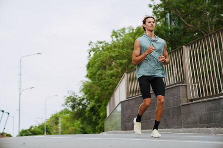 Young handsome athletic long-haired man in headphones running outdoors