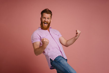 Ginger white man with beard screaming and winner gesture isolated over pink backgroundの写真素材