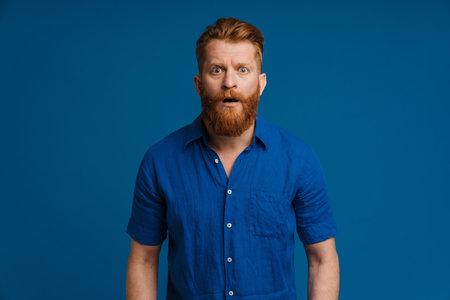 Ginger white man with beard expressing surprise at camera isolated over blue backgroundの写真素材