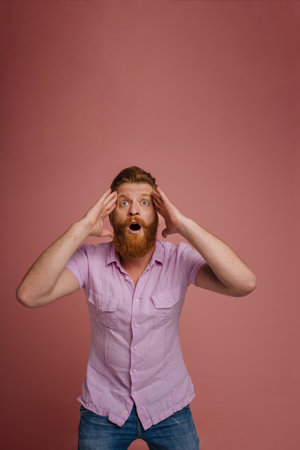 Ginger white man with beard expressing surprise at camera isolated over pink background