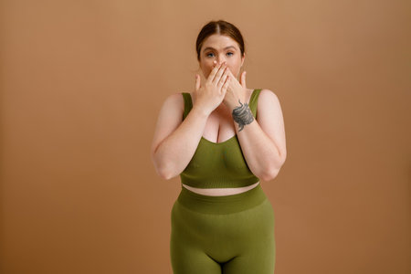 White young woman with ginger hair posing while covering her mouth isolated over beige backgroundの写真素材