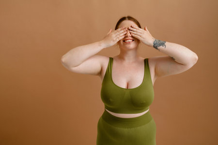 White young woman with ginger hair smiling and covering her eyes isolated over beige backgroundの写真素材