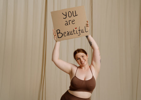 White woman smiling and gesturing while showing placard isolated over beige backgroundの写真素材