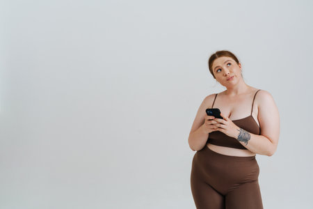 European puzzled woman with ginger hair using mobile phone isolated over white backgroundの写真素材